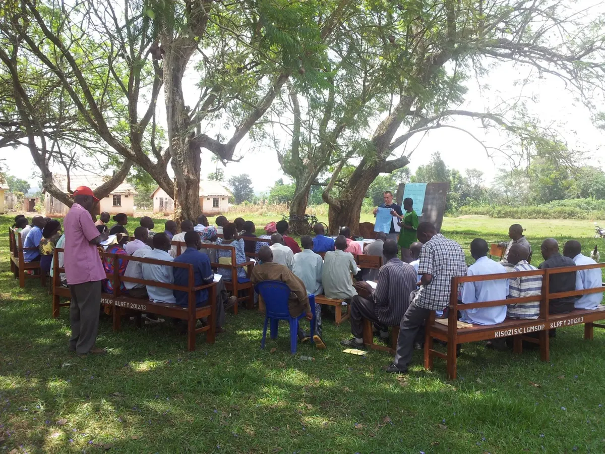 About forty cooperative members on benches under the trees, facing a flip chart